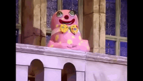 a pink clown is standing on a balcony wearing a bow tie and a clown mask .