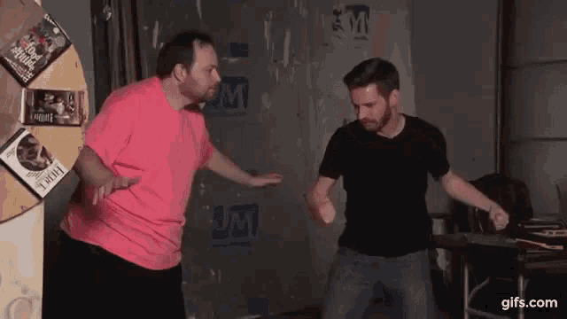 a man in a pink shirt is standing next to another man in a black shirt in a room .