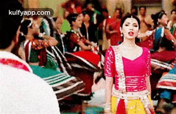 a woman in a pink and yellow dress is dancing in front of a crowd .