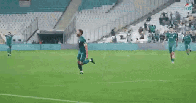 a soccer player is celebrating a goal on a soccer field with a stadium in the background .