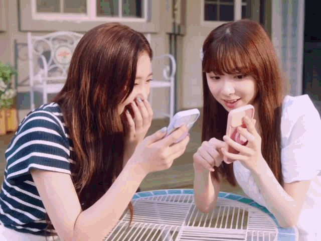 two girls sitting at a table looking at their cell phones