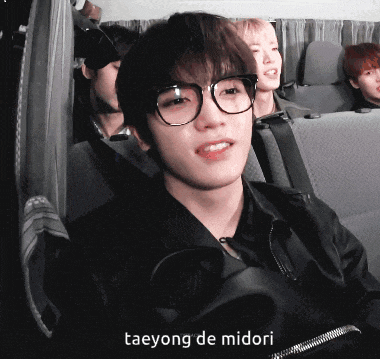 a young man wearing glasses is sitting in a car with the name taeyong de midori written below him