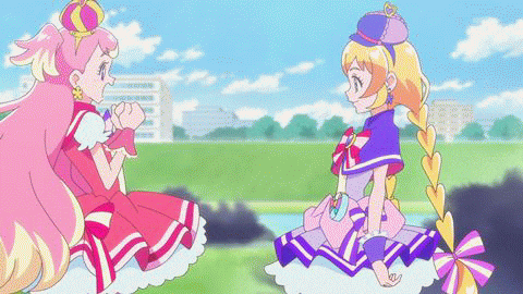 two anime girls are sitting next to each other in a field and talking to each other .