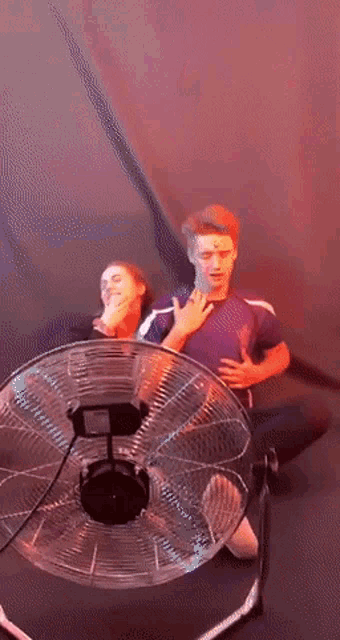 a man and a woman sit in front of a fan