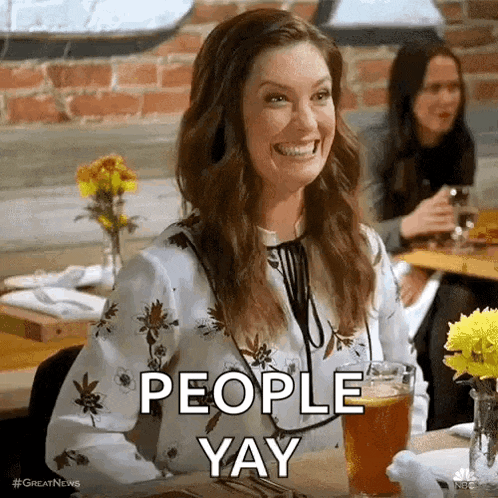 a woman is smiling while sitting at a table with a glass of beer and the words `` people yay '' .