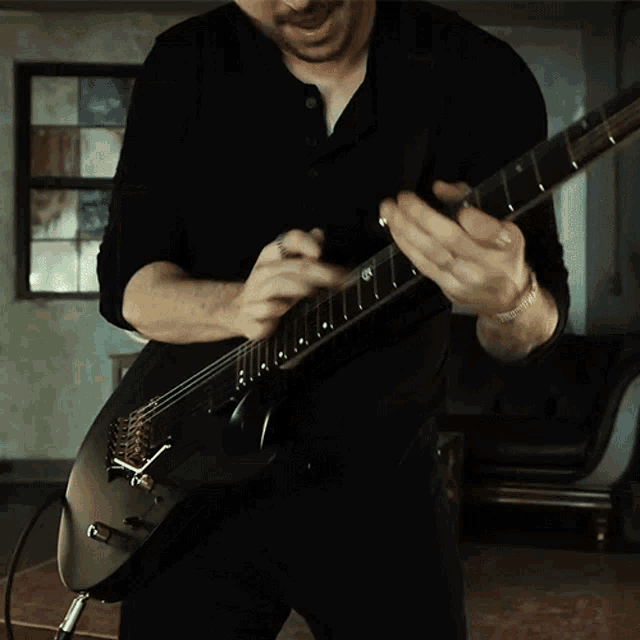 a man in a black shirt is playing a black guitar in a dark room