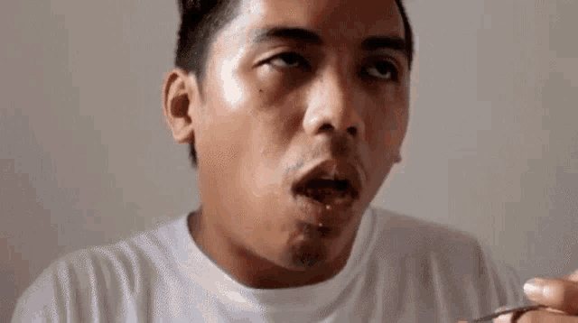 a man in a white shirt is eating a piece of food with a knife and fork .