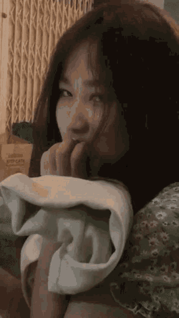 a woman is laying on a bed with a towel around her neck and covering her mouth with her hand .