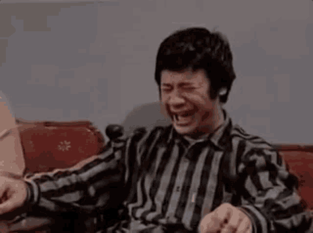 a man is sitting on a couch laughing with his eyes closed .