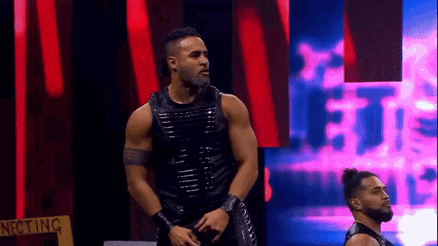 two wrestlers are standing on a stage in front of a pink and red background .