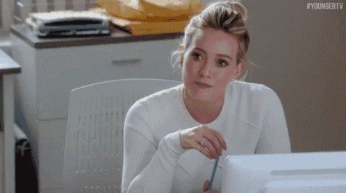 a woman in a white sweater is sitting in front of a computer screen .