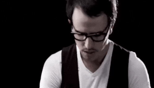 a man wearing glasses and a white shirt looks down
