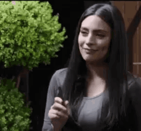 a woman with long black hair is smiling and holding a cigarette .