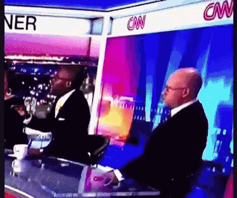 a man in a suit and tie is sitting in front of a cnn sign