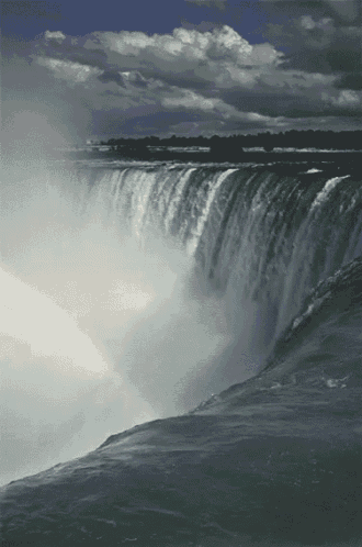 a waterfall with a rainbow in the background on a cloudy day