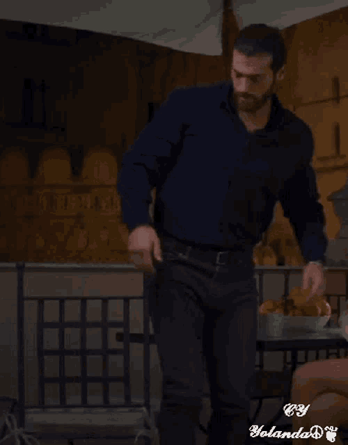 a man in a blue shirt and black jeans is standing in front of a table with food on it .