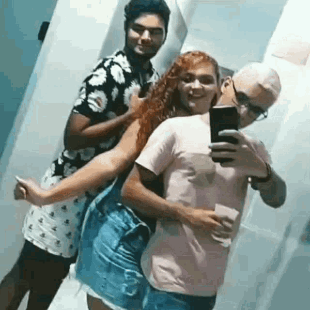 a man is taking a selfie with two women in a bathroom while a woman holds a man 's arm .