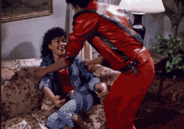 a man in a red jacket holds a woman on a couch