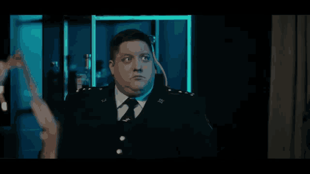 a man in a police uniform is standing in a dark room with a blue light behind him .