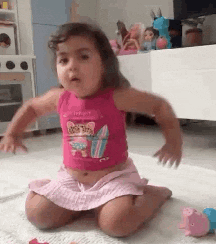 a little girl is sitting on the floor with her arms outstretched in a living room .