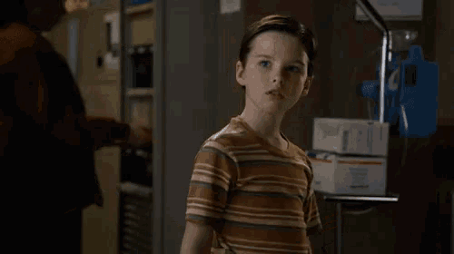 a young boy in a striped shirt is standing in a room with a woman standing behind him .