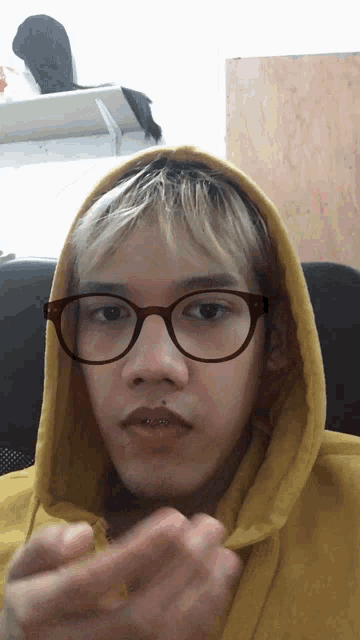 a man wearing a yellow hoodie and glasses looks at the camera