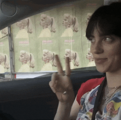 a woman in a car giving a peace sign in front of a poster that says ' i love you '