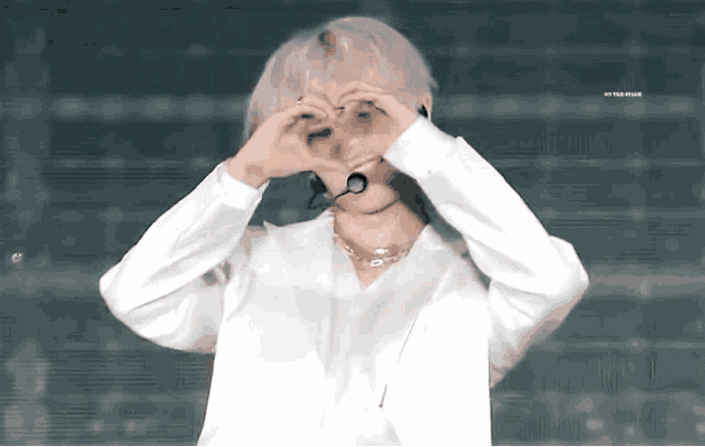 a man with white hair is making a heart shape with his hands .