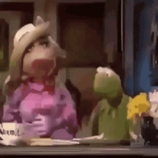 miss piggy and kermit the frog are sitting at a table .