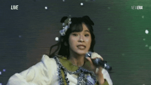 a woman is singing into a microphone while wearing a flower in her hair .