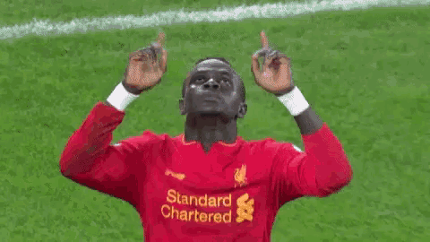 a soccer player wearing a red shirt that says standard chartered is giving a thumbs up sign .