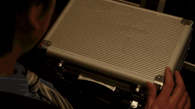 a man in a blue shirt and tie is holding an aluminum case