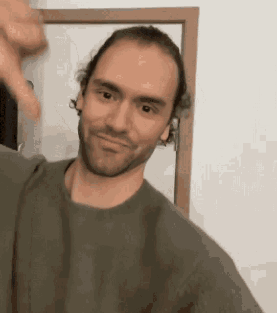 a man with a beard is giving a thumbs down sign while standing in front of a mirror .