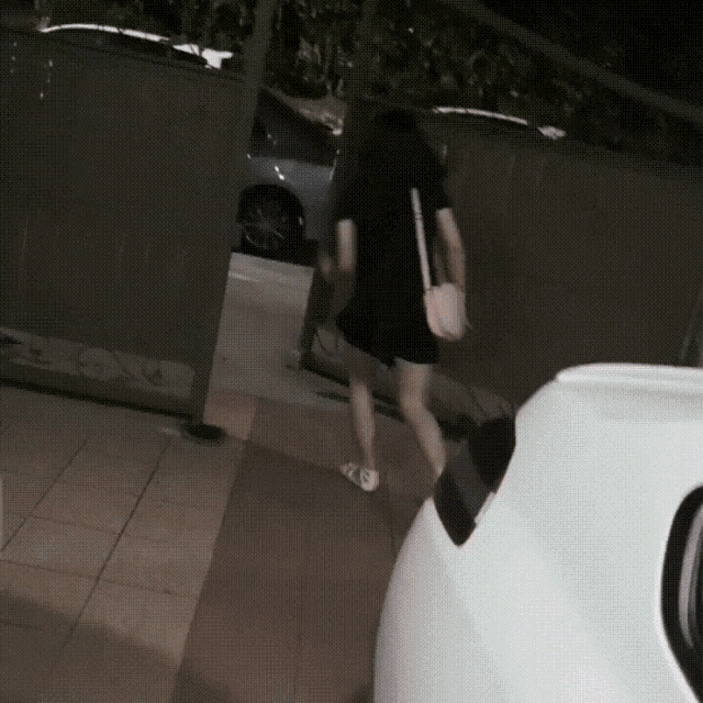 a woman in a black dress is walking down a sidewalk near a white car