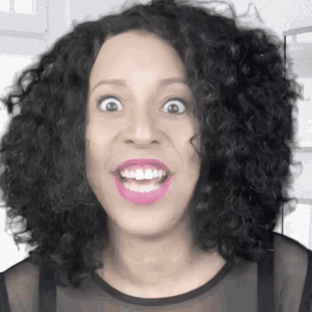 a woman with curly hair is making a funny face and smiling .