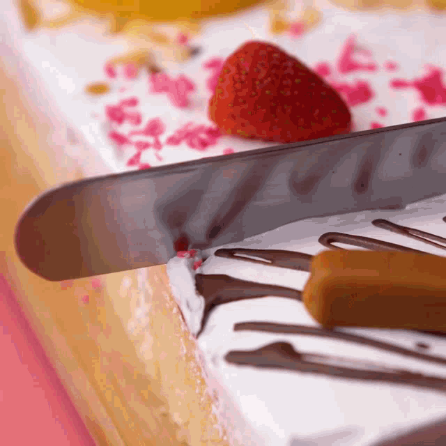 a knife is being used to cut a cake with strawberries on top