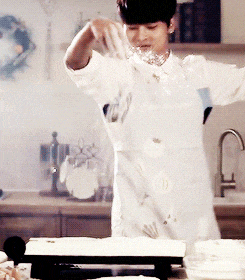 a man in a white apron is pouring something on a table in a kitchen