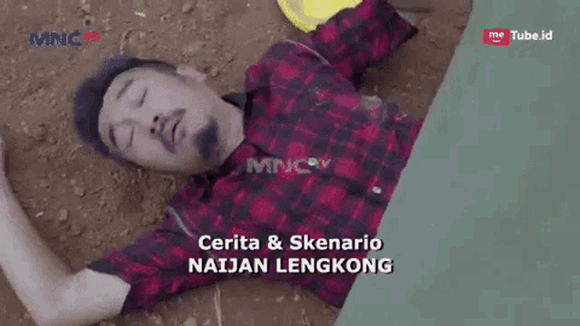a man in a plaid shirt is laying on the ground in the dirt .