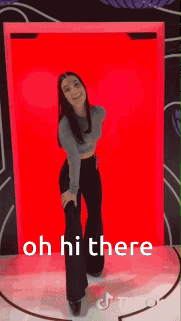 a woman is standing in front of a red wall with the words oh hi there written on it