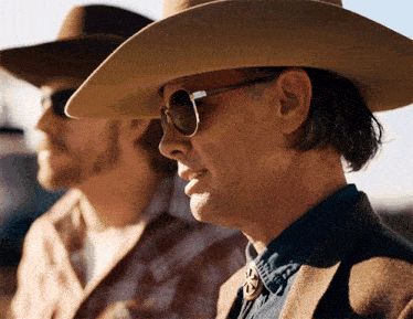 a man wearing a cowboy hat and sunglasses stands next to another man wearing a plaid shirt