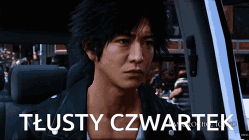 a man sitting in a car with the words tlusty czwartek written on the screen