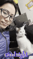 a woman wearing glasses is sitting next to a white cat with the words goodnight written on it .