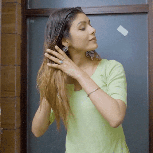 a woman in a green shirt is brushing her hair in front of a mirror