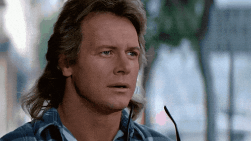 a man with a mullet and glasses looks at something
