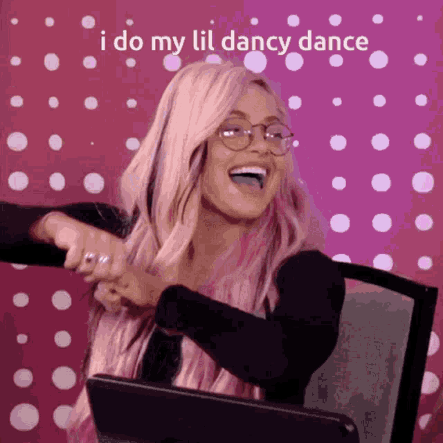 a woman with pink hair and glasses says i do my lil dancy dance while sitting in a chair
