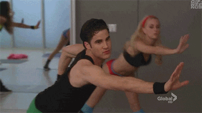 a man in a black tank top is doing squats with a woman in a red bra behind him