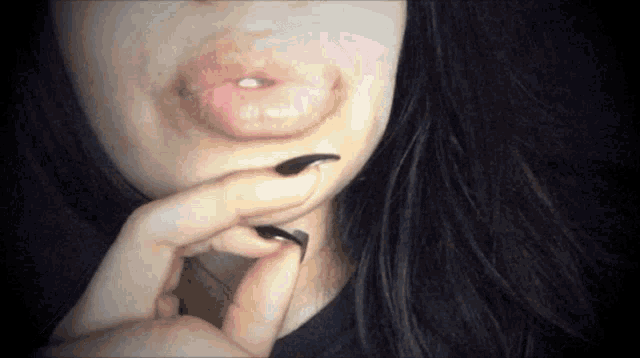 a close up of a woman 's face with black nails and a piercing in her lip