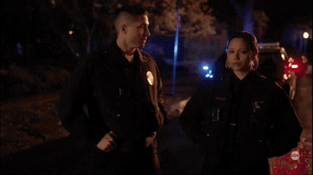 a man and a woman are standing next to each other in front of a police car at night