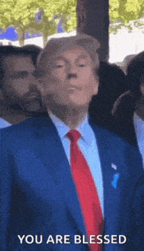 donald trump is wearing a blue suit and red tie and is standing in front of a crowd .