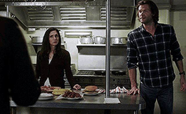 a man and a woman are standing in a kitchen looking at food
